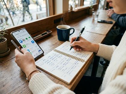 ノートに条件を書き出してアプリを比較検討している女性の手元