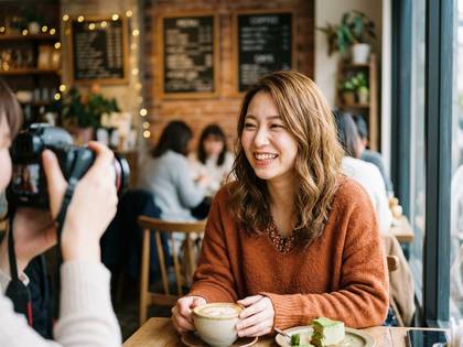 カフェで笑顔の女性がコーヒー片手に写真撮影される。