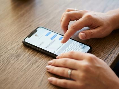 スマホでメッセージのやり取りをしている女性の手元クローズアップ。木目調のテーブル。800×600