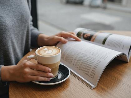 カフェで雑誌を読みながらラテを飲む女性の手元