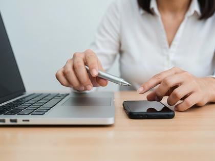 ノートパソコンとスマホを並べてアプリを比較検討している女性の手元