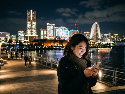 横浜の夜景を背景にスマホ画面を見ながら笑う20代女性