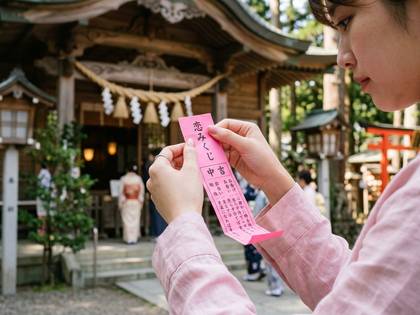 神社でピンク色の恋みくじを読む女性の横顔と手元。