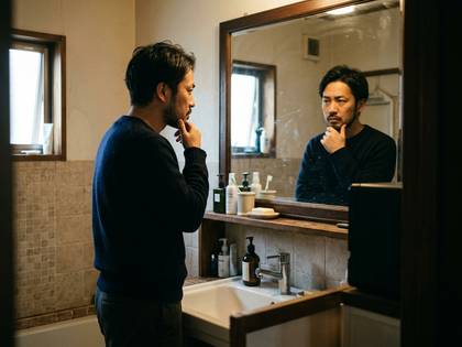 洗面所の鏡に映る、顎に手を当てて物思いにふける男性。