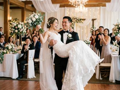 新郎が新婦を抱きかかえ、幸せな笑顔を見せる結婚式の様子。