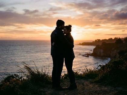 夕焼けの海を背景に、額にキスするカップルのシルエット。