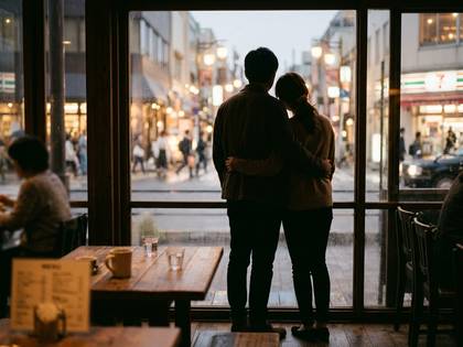 カフェの窓から街を眺める抱き合うカップルの後ろ姿。