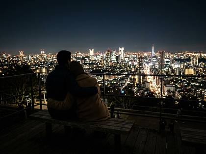 東京の夜景を眺め、ベンチで寄り添うカップル。