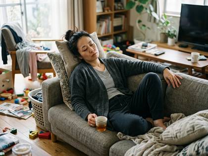 散らかったリビングのソファで眠る、疲れ切った女性。
