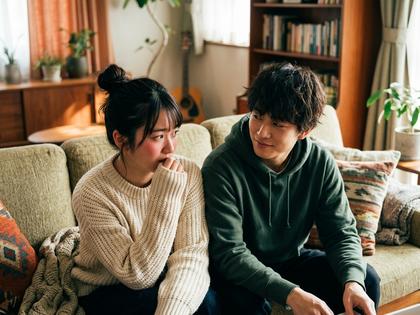 ふたりでソファに並んで座り、片方が照れた表情でそっぽを向いているシーン