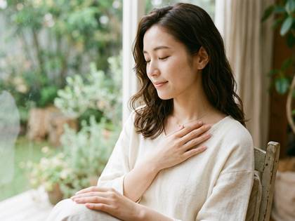 窓辺で穏やかに目を閉じ、胸に手を当てる女性。