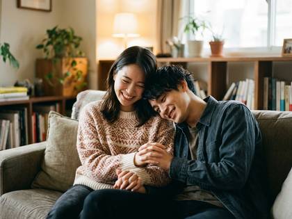 温かいリビングでソファに座り、笑顔で寄り添う若いカップル。