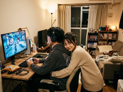 ゲーム中の男性に、笑顔で寄り添う女性カップル。