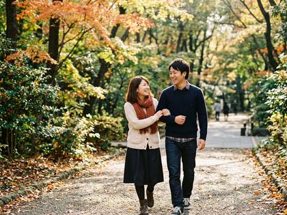 紅葉が美しい公園の小道を笑顔で歩くカップル。