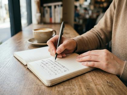 ノートにプロフィール文を書き出している女性の手元アップ
