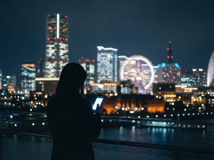 横浜の夜景を背景にスマホを見つめる女性のシルエット写真