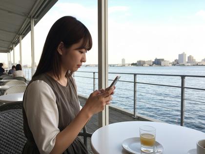 横浜の海沿いカフェでスマホを操作する女性の写真