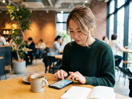 カフェでスマホを操作しながらアプリを試している20代女性の様子