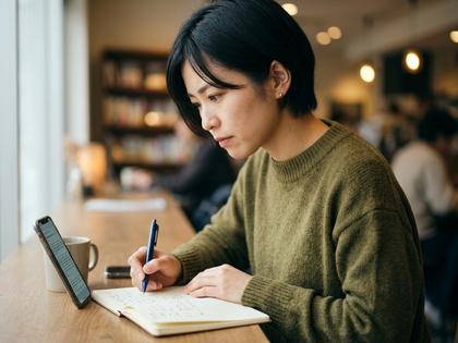 ノートにメモを取りながらスマホ画面を真剣に見つめる女性、考え事をしている雰囲気