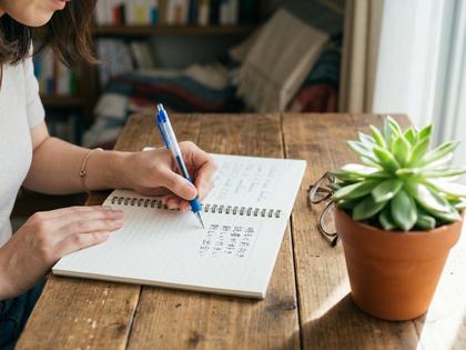 ノートにプロフィール文を書き込んでいる女性の手元、観葉植物がそばにある