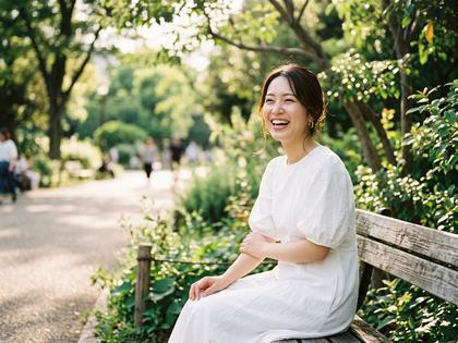 公園で友人に撮ってもらった自然な笑顔の女性。ナチュラルメイク、白いワンピース