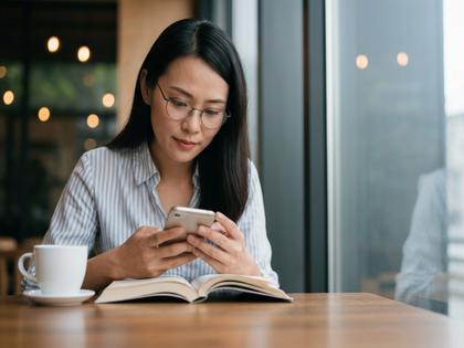 カフェで本を読みながらスマホをチェックする40代女性
