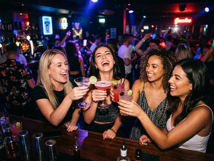 クラブでカクテルグラスを掲げて笑う若い女性グループのイメージ