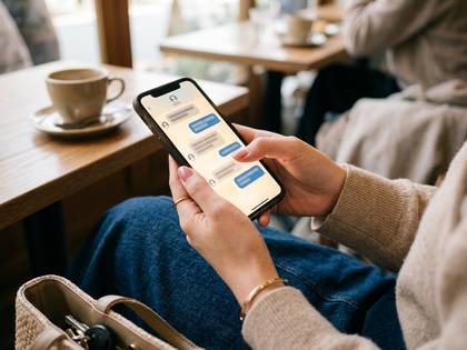 カフェでスマートフォンを操作する女性の手元。チャット画面が表示されている。