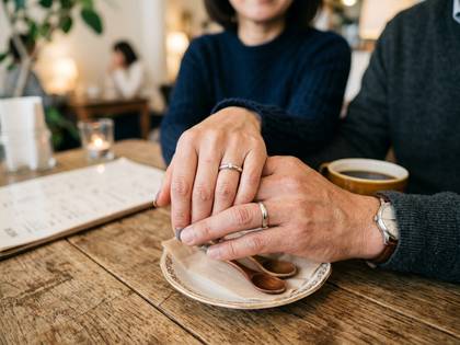 カフェで指輪をつけた夫婦が手を取り合う。