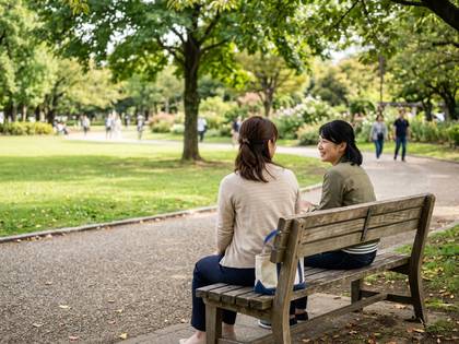 公園のベンチで笑顔で談笑する2人の女性。豊かな緑の背景。