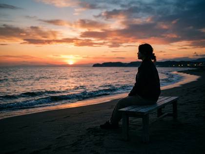 夕暮れのビーチでベンチに座り、海と夕日を眺める女性のシルエット。