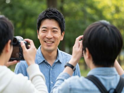 公園で友人に撮ってもらっている自然な笑顔の男性のイメージ