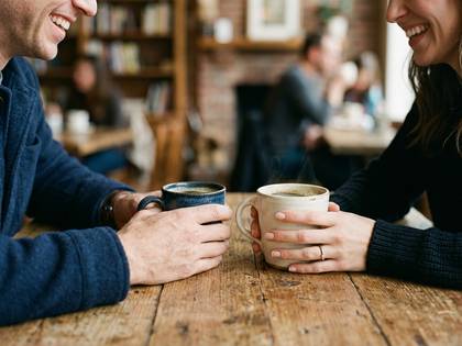 カフェで笑顔でコーヒーを飲む男女の手元。
