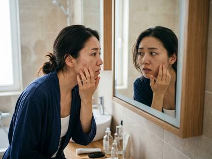 浴室で鏡を見て肌の悩みを心配そうに触る女性。
