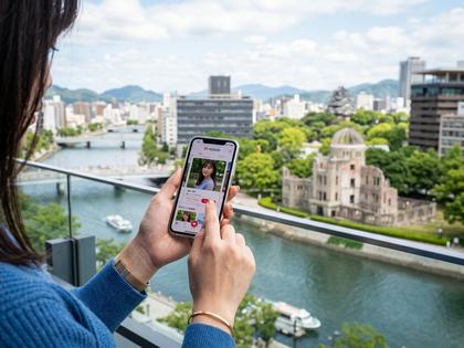 広島市の街並みとスマートフォンでマッチングアプリを操作している女性の手元