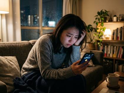 深夜、ソファでうつむきながらスマホ画面を見つめる女性。