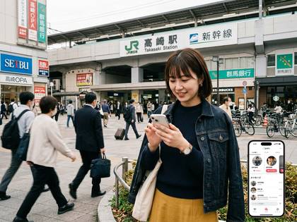 JR高崎駅を背景に、スマートフォンを操作する笑顔の若い女性。