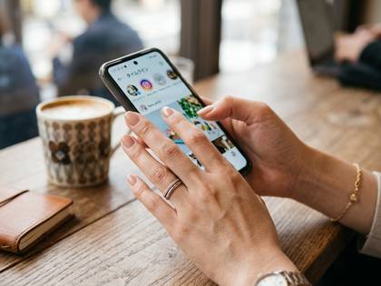 カフェで女性がスマートフォンを操作し、SNSのタイムラインを閲覧中。
