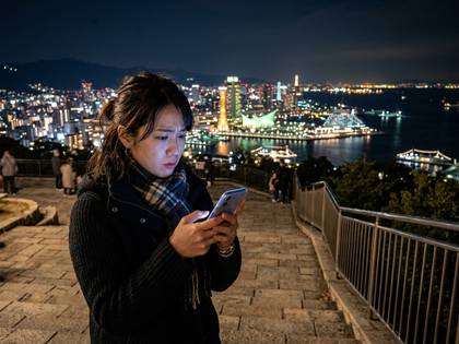 夜景を背景にスマートフォンを見つめる女性。
