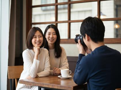 カフェで自然な笑顔の女性を友人が撮影しているシーン