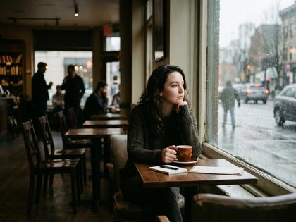 カフェの窓辺で一人スマホを見つめる女性の後ろ姿、柔らかな自然光