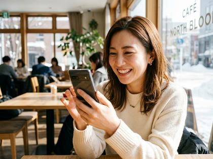 カフェで自然な笑顔の女性がスマホを見ているイメージ