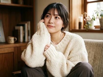 オーバーサイズニットの萌え袖で頬に手を当てる女性の写真