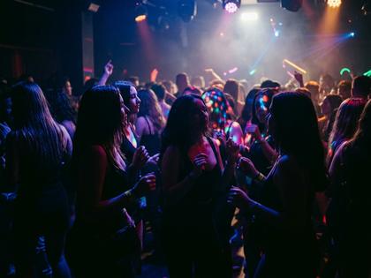 薄暗いナイトクラブのフロアで音楽を楽しむ若い女性たちの後ろ姿、照明が光っている様子