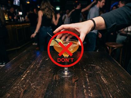 クラブのテーブルに置かれたカクテルグラスと、それを手に取ろうとする女性の手