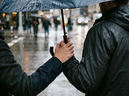 傘の柄を持つ男性の手と、少し内側に傾いた傘。男性側の肩が雨で濡れている様子のアップ